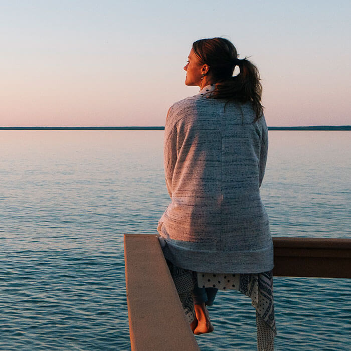 woman looking out at waterfront while sitting on railing