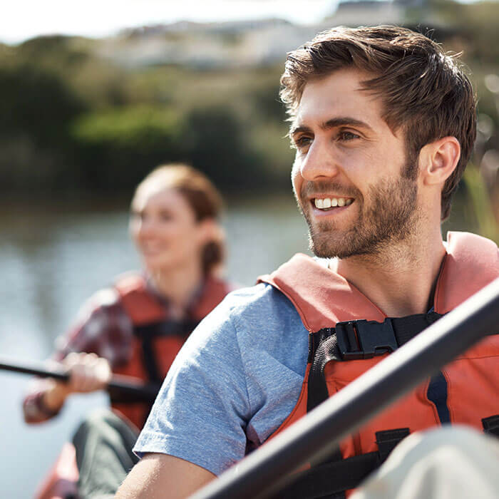 man smiling on kayak with woman behind him