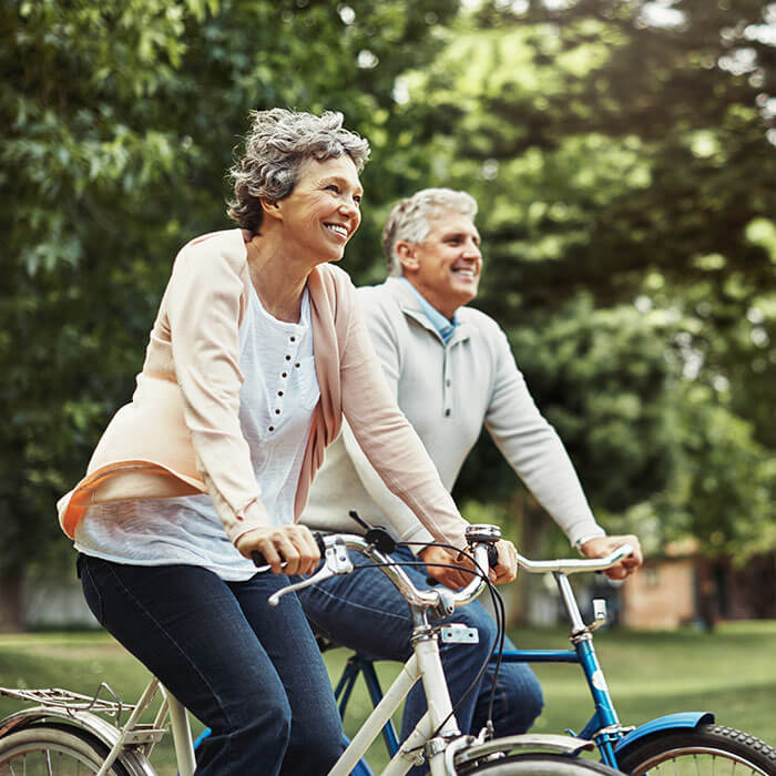 mature woman and man riding bikes together under trees