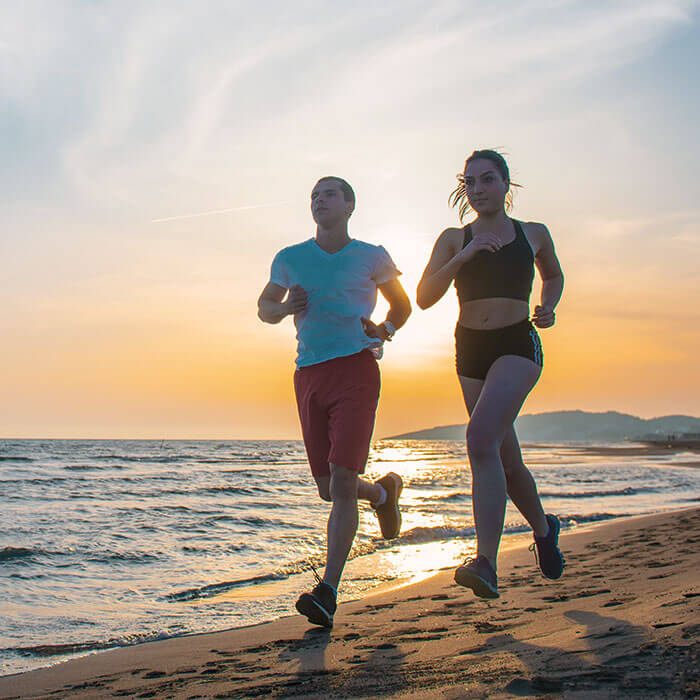 man and woman running on the beach together at sunrise