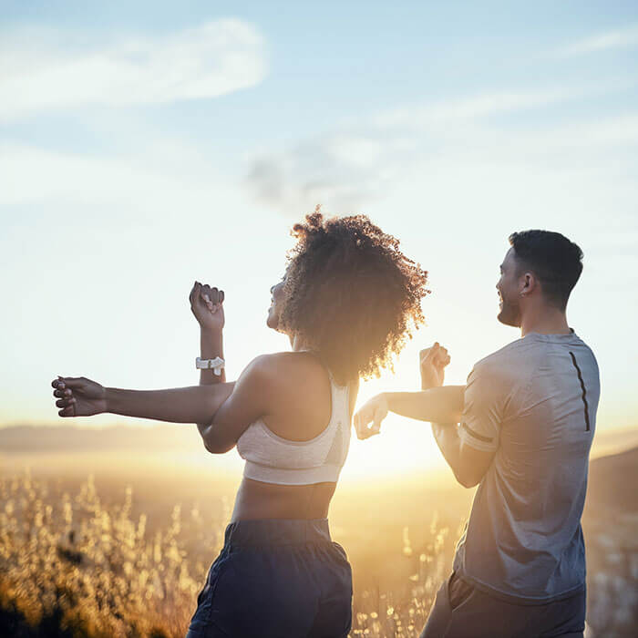 man and woman stretching arms while looking at sunset