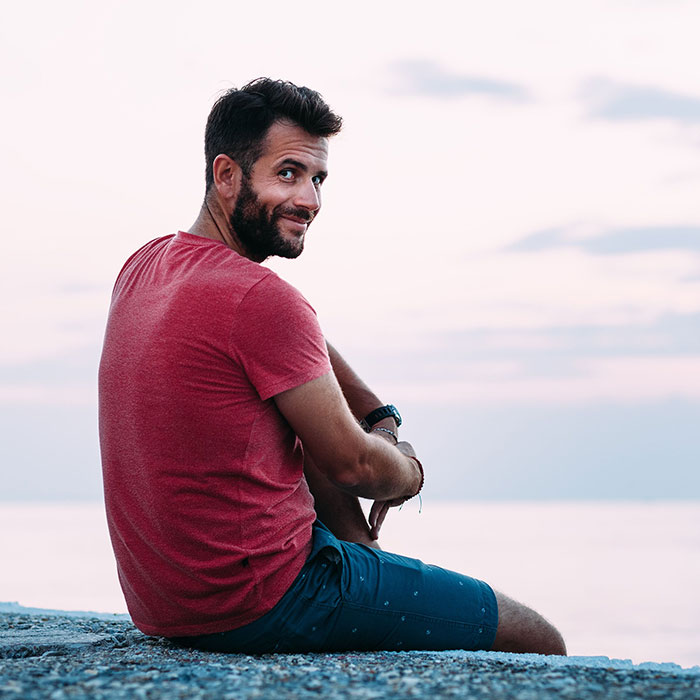 smiling man sitting on edge of pavement near beach