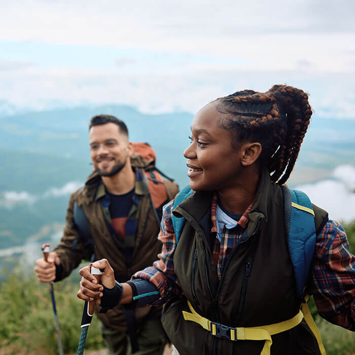woman hiking on cloudy mountain with partner following behind her